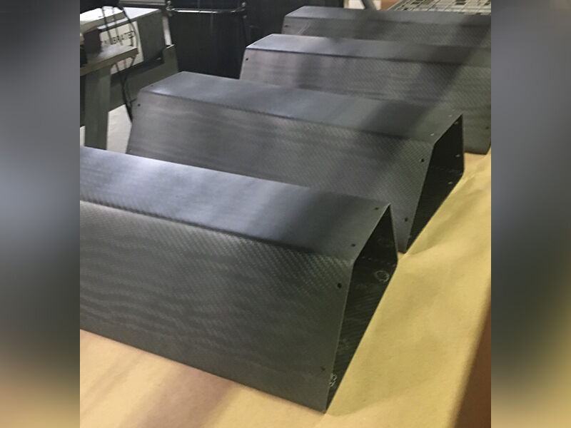 Carbon fiber sensor enclosures in a row laying on a flat surface in an office space. The enclosures have a trapezoidal cross sections. The surfaces are matte carbon fiber weave.